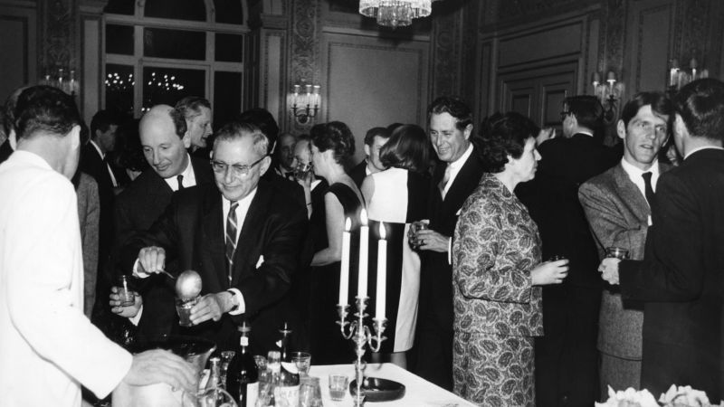 Black and white photo from 1966 showing various men and women socializing in a room in a Roman villa