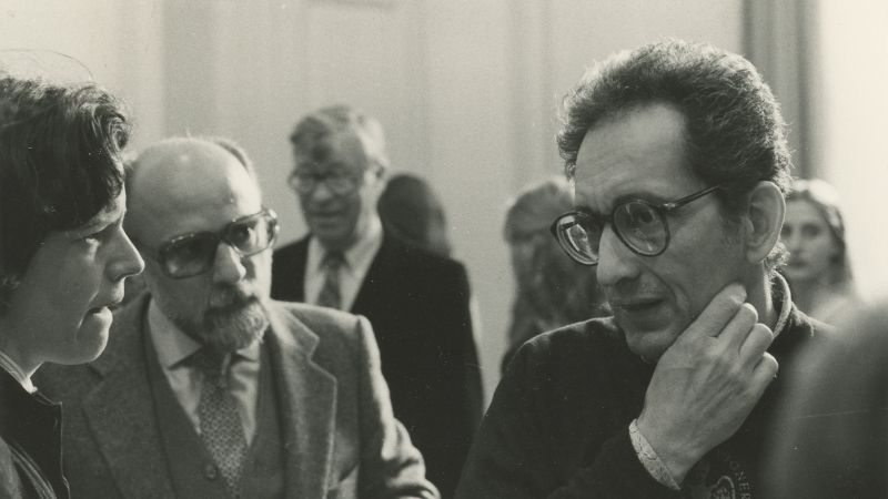 Black and white photo of the heads and shoulders of two men and one women in conversation