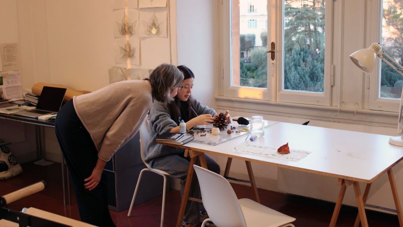 Color photo of an adult and child sitting at a work table