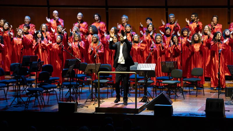 A man conducts a large choir in red robes