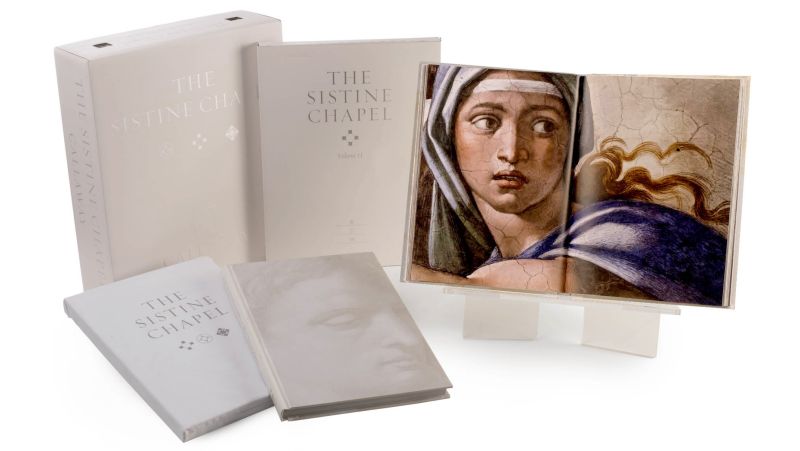 Color photograph of three books with white covers, a white slipcase for the books, and a book open to a page showing a color reproduction of a fresco in the Sistine Chapel