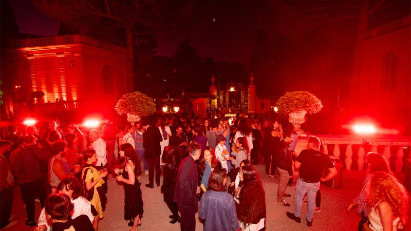 Color photo of people standing and having conversations in a villa entrance bathed in red light
