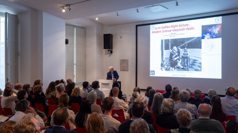 Color photo of a man speaking at a lectern in a full lecture room