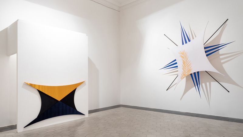 Color photograph of two star-shaped abstract sculptures hanging on white walls
