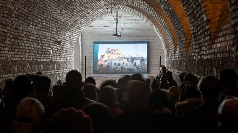 Color photograph of the backs of people's heads as they watch a video screening in a barrel vaulted room