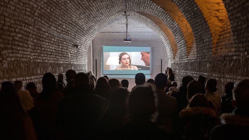 Color photograph of the backs of people's heads as they watch a video screening in a barrel vaulted room