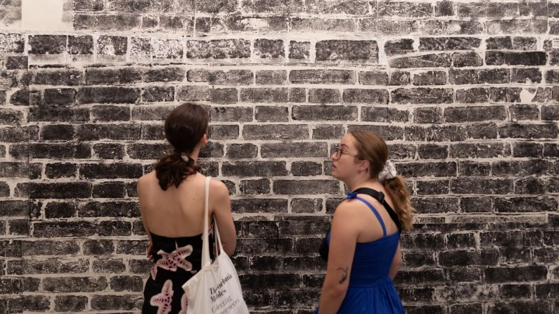Two people look at a life-sized print of stone making up a tower on the great wall of China
