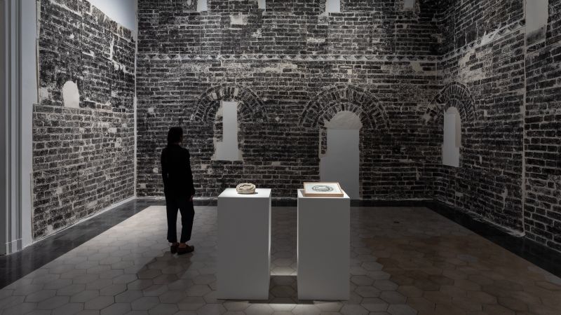 A woman stands in a gallery with a print of the Great Wall of China surrounding her