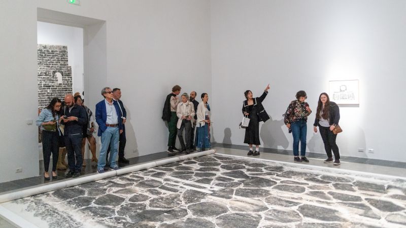 May visitors in front of a large art installation that is a print of the Appian Way