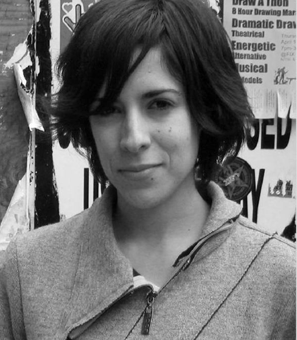 Black and white photograph of the head and shoulders of a light skinned woman with dark hair looking at the camera