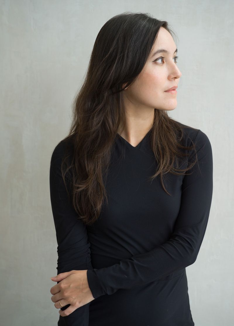 Color portrait of Alexandra Kleeman from the waist up and wearing a black dress, with her body facing forward and her head turned to her left