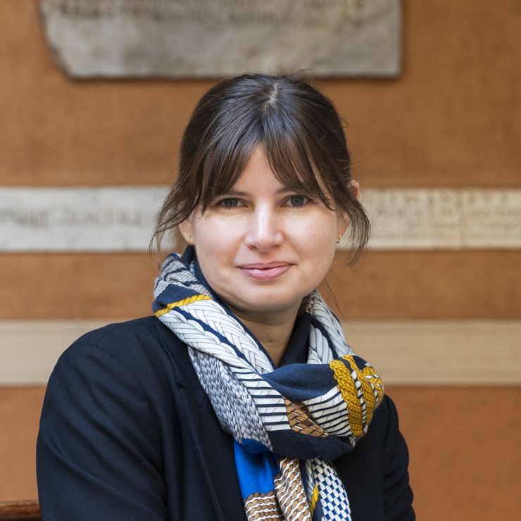 Color photograph of the head and shoulders of a light skinned woman in an Italian courtyard