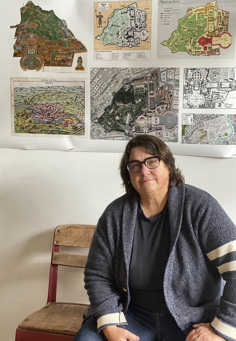 Catherine Opie sits in a chair underneath maps of Vatican City affixed to the wall behind