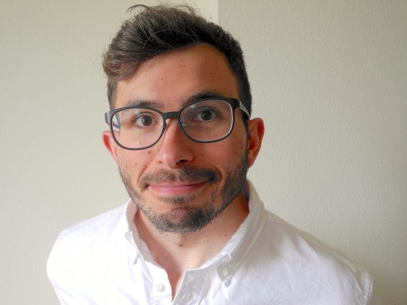 Color portrait of the head and shoulders of Danny Smith, wearing glasses and a white open-collared shirt and facing forward