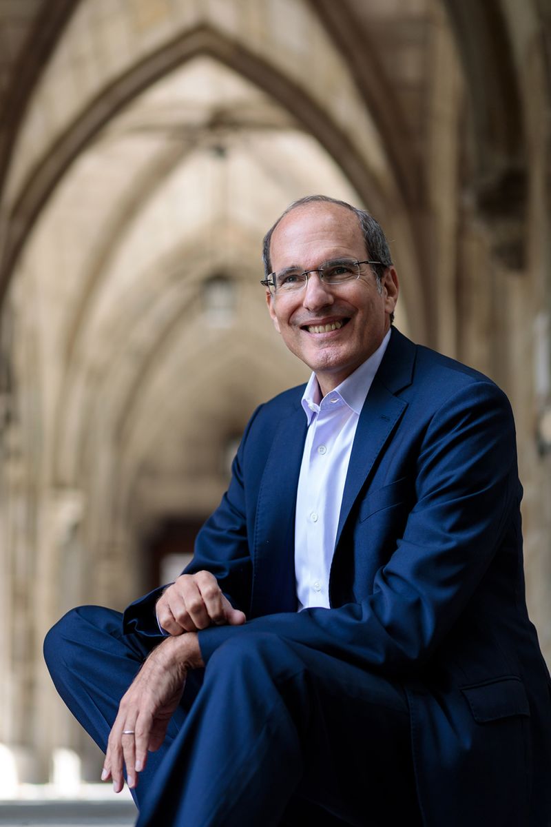 Color photograph of David Nirenberg sitting outside the cloister connecting Swift Hall to Bond Chapel at the University of Chicago