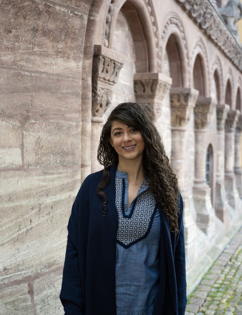 Color photograph of Erene Rafik Morcos standing outdoors alongside medieval architecture