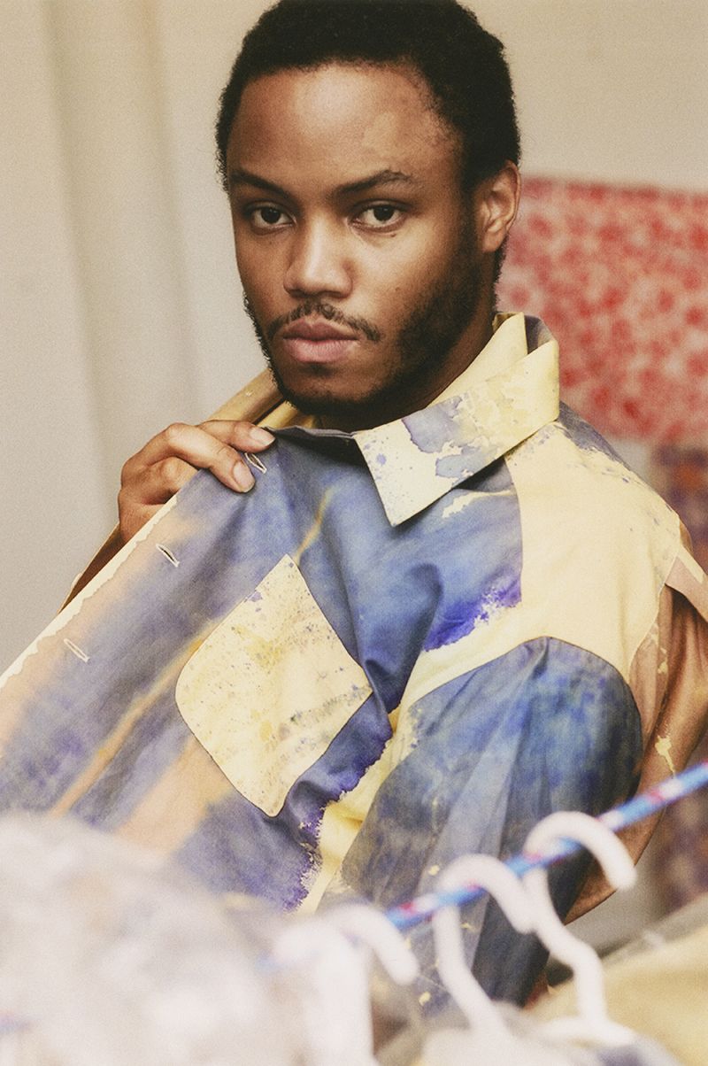 Color photograph of the head and torso of Eric N. Mack, holding a shirt-like garment to his body