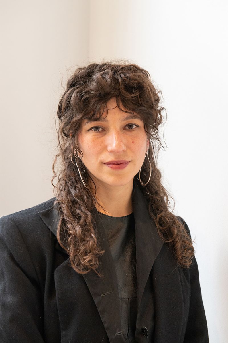 Color photograph of a light skinned woman wearing a black blazer and shirt looking at the camera with a serious expression