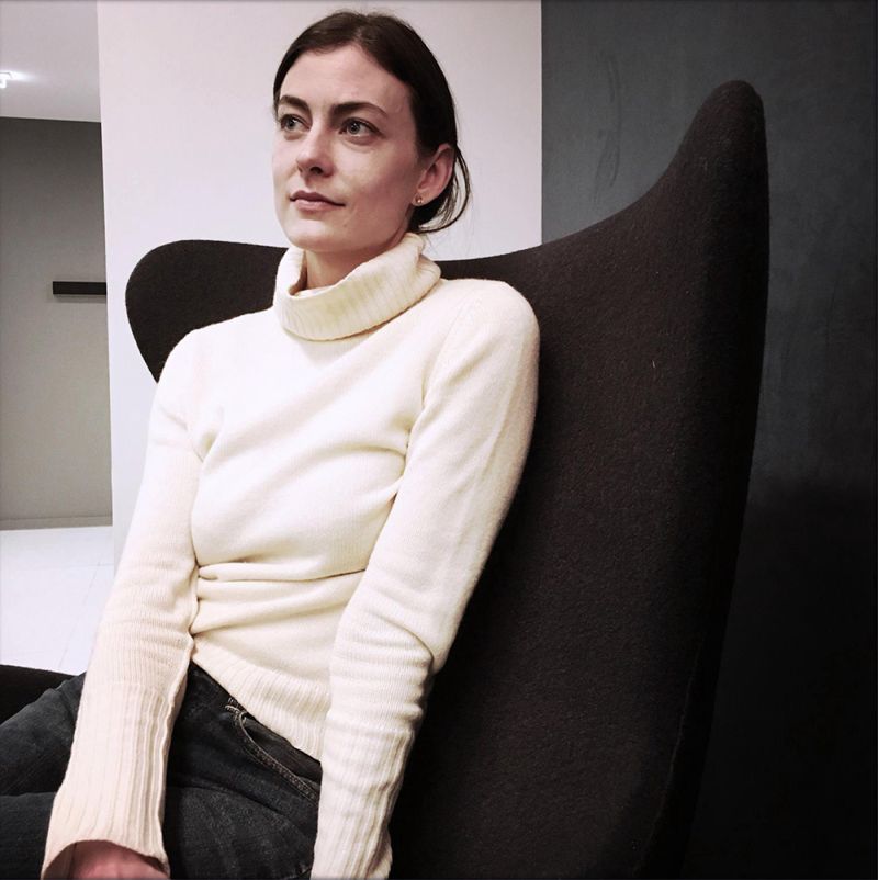 Color photograph of Jennifer Pastore, sitting in a modernist chair in a 3/4 pose