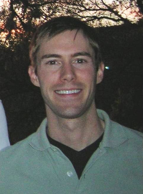 Color photograph of the head and torso of a light skinned man wearing a green polo shirt and smiling at the camera