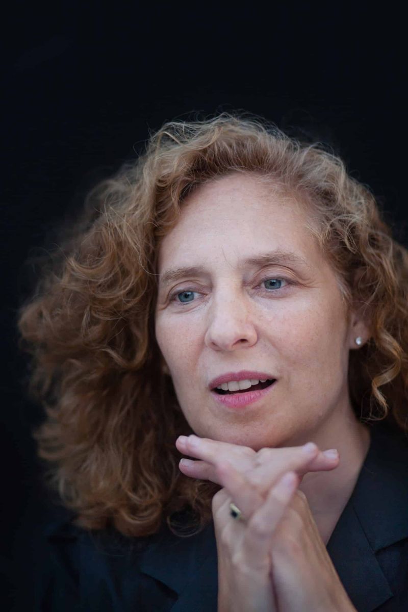 Color photo of the head and shoulders of a light skinned woman with reddish hair looking at the camera
