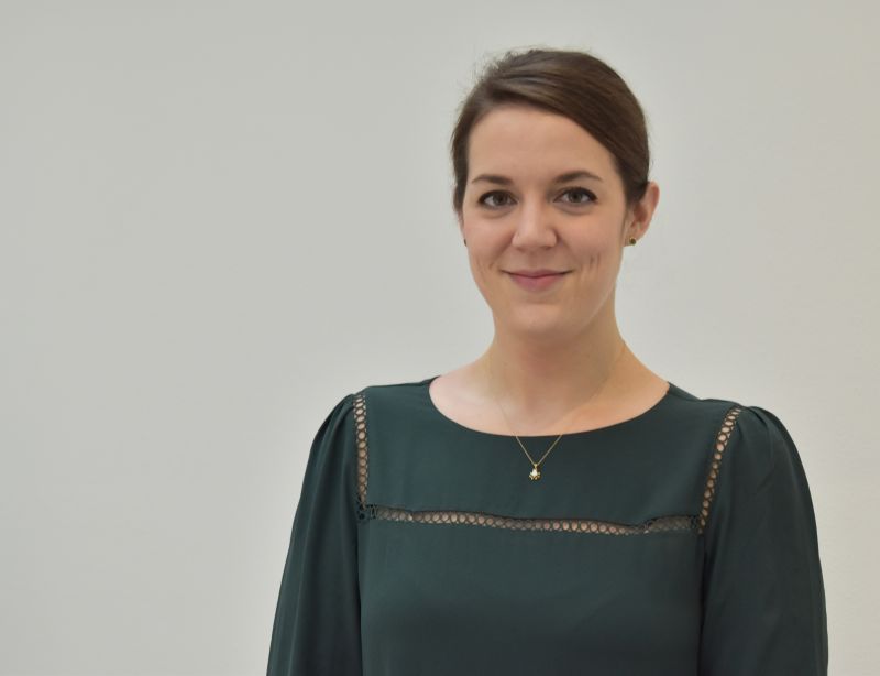 Color portrait of Lindsay Sheedy from the waist up, wearing a dark green dress, facing forward, and standing against a neutral gray background
