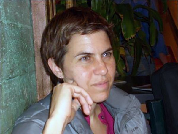 Color photograph of the head and shoulders of a light skinned man with her hand on her cheek; she looks off camera
