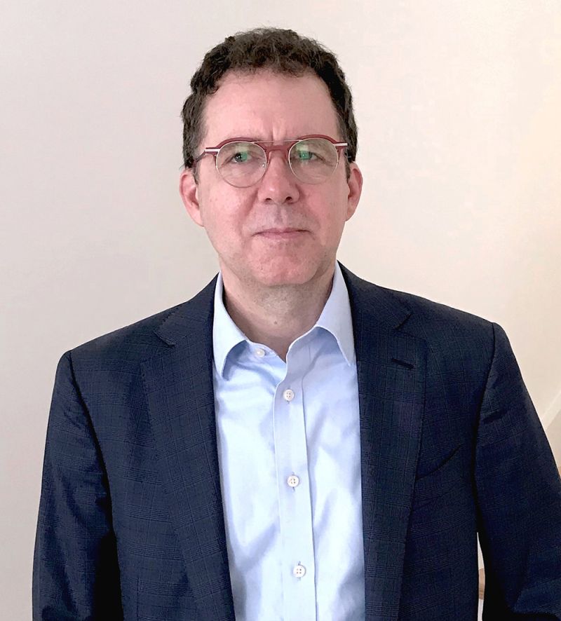 Color photograph of the head and torso of Michael Lee wearing a suit jacket and standing in front of a white wall
