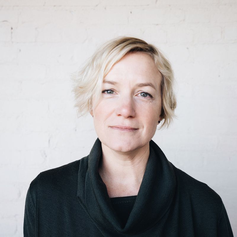 Color photograph of the head and shoulders of Phoebe Lickwar, facing forward against a white wall
