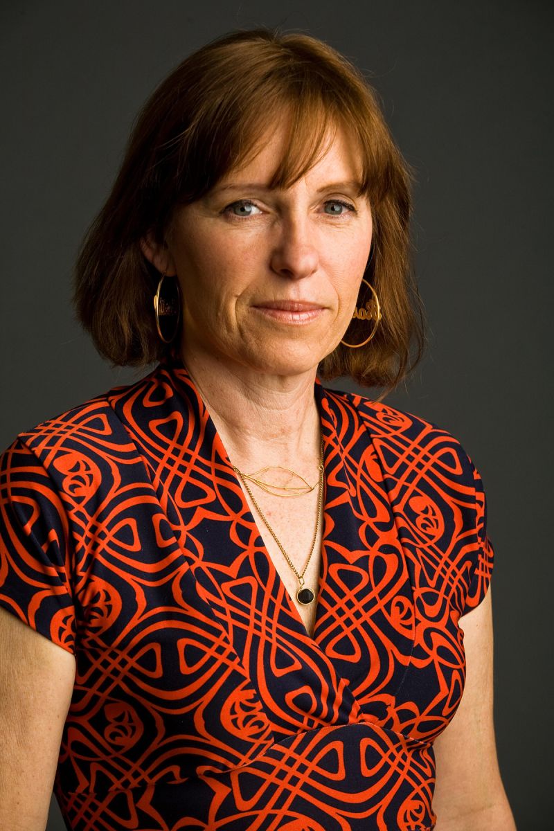 Color photograph of the head and torso of a light skinned woman in a photographer's studio wearing a red and black abstract patterned top