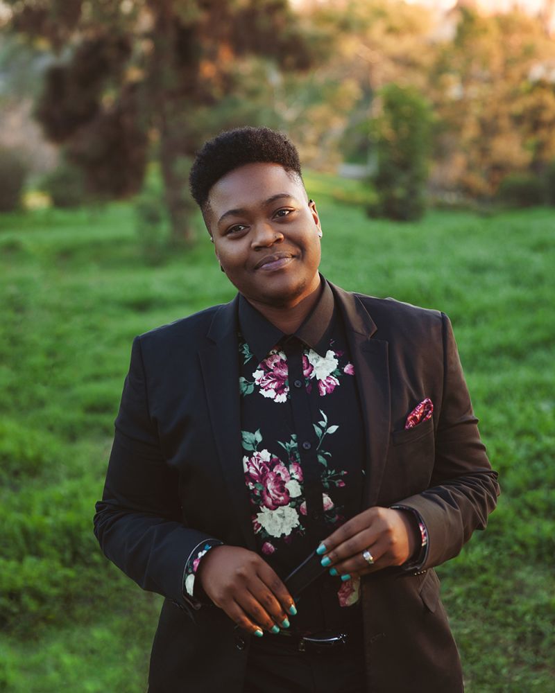 Color photograph of SA Smythe, standing outside in a sharp suit against a lush green background
