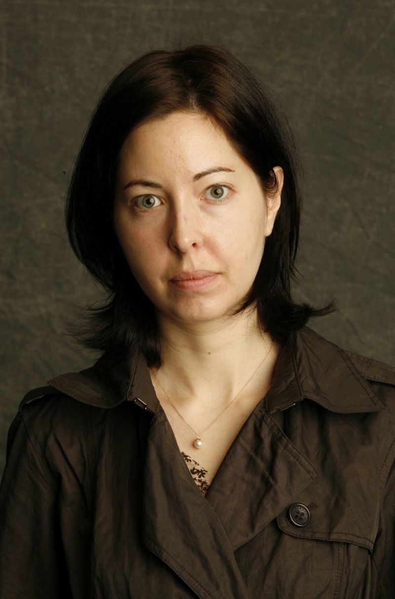 Color photograph of the head and torso of a light skinned woman with dark hair looking at the camera with a serious expression
