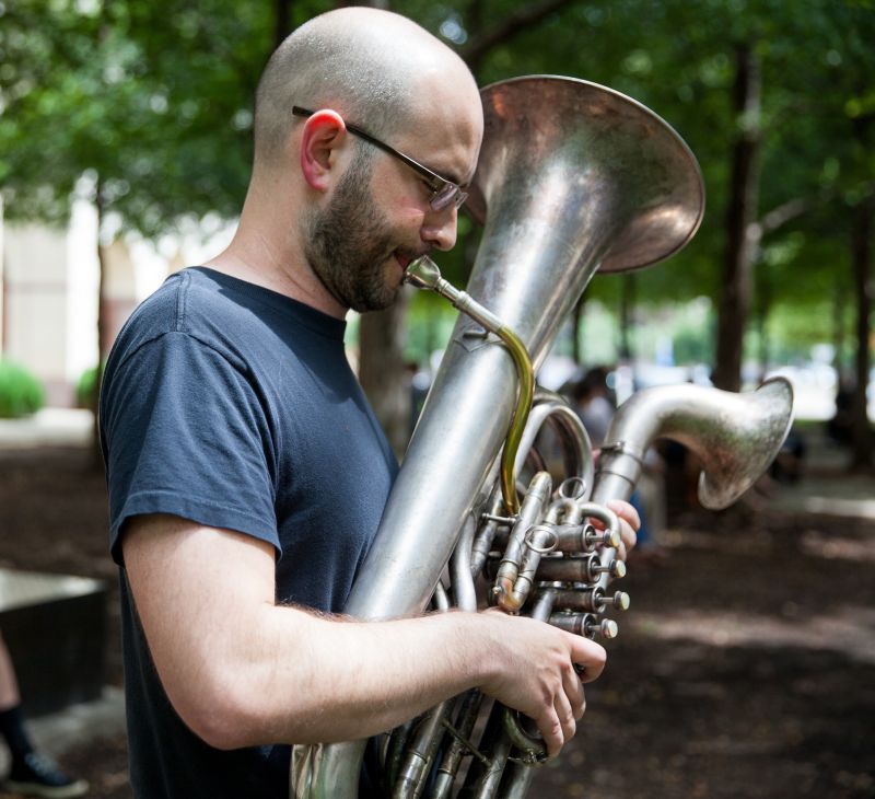 Color profile portrait of Steven Parker from the waist up, playing a brass instrument that looks like a euphonium