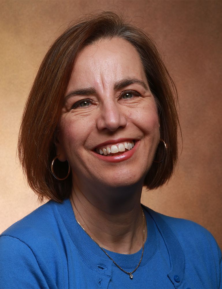 Color photo of a woman smiling at the camera against a studio backdrop