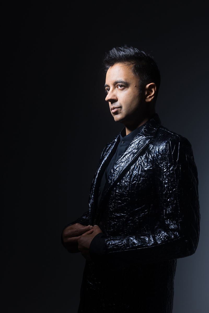 Color portrait of a brown skinned Indian man wearing a crinkly black jacket and looking off camera