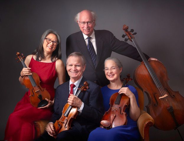 Color portrait photograph of four elderly people holding stringed instruments against a gray studio backdrop