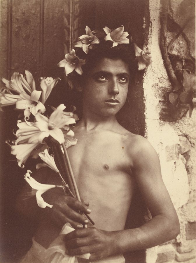 Monochromatic brown 19th-century photograph of the head of a young boy wearing a floral crown and staring off camera